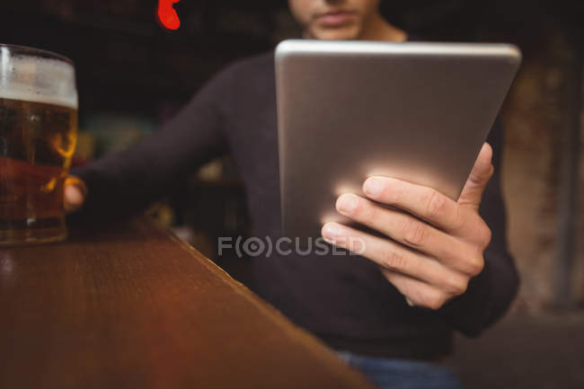 Homem com copo de cerveja usando tablet digital no balcão no bar — Fotografia de Stock