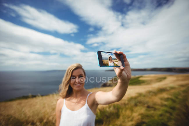 Donna sorridente scattare selfie con smartphone in campo — Foto stock