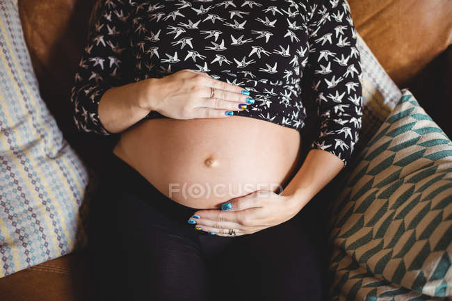 Imagem cortada da mulher grávida relaxante e comovente barriga na sala de estar — Fotografia de Stock