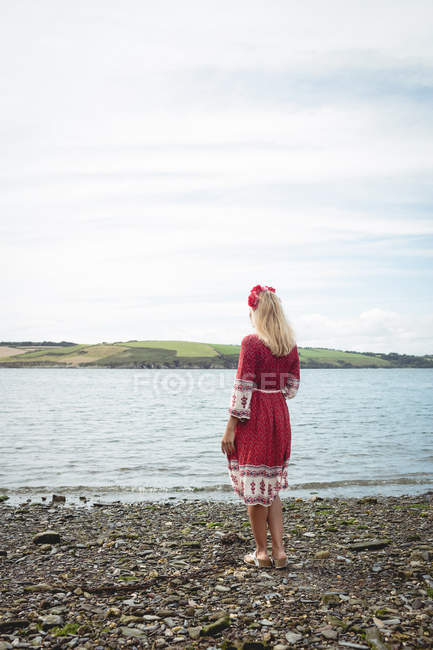 Back view of blonde woman in red dress standing near river — Stock Photo