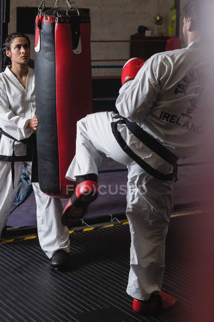 Luchadores practicando karate con saco de boxeo en estudio - foto de stock