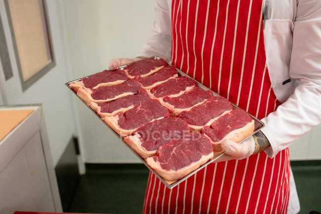 Mid section of butcher holding a tray of steaks at butchers shop — Stock Photo