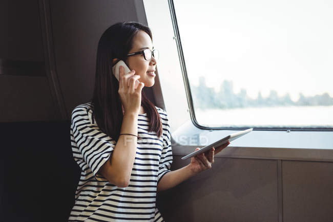 Junge Frau schaut durchs Fenster, während sie mit dem Handy spricht — Stockfoto