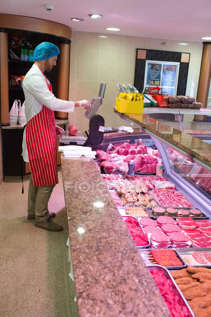 Macellaio che controlla il peso della carne al banco in macelleria — Foto stock