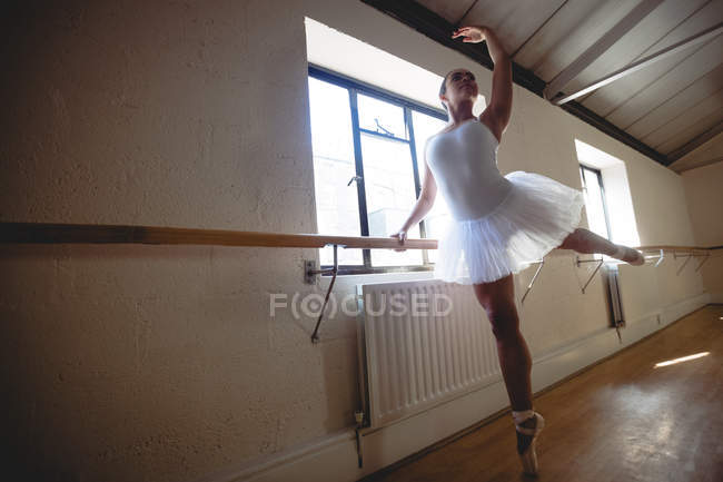 Low angle view of Ballerina practicing ballet dance at barre in studio — Stock Photo