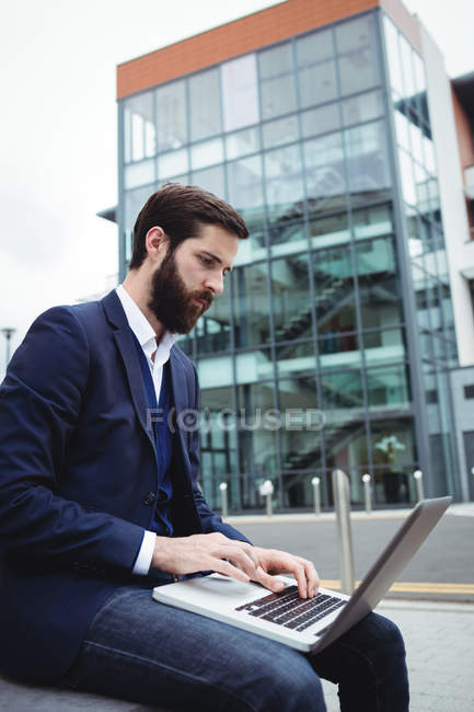 Attentive businessman using laptop outside office — Stock Photo