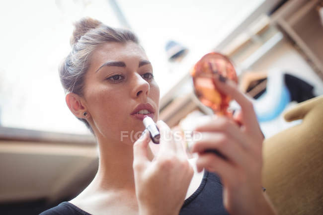 Mujer que aplica lápiz labial mientras mira el espejo pequeño en la tienda boutique - foto de stock