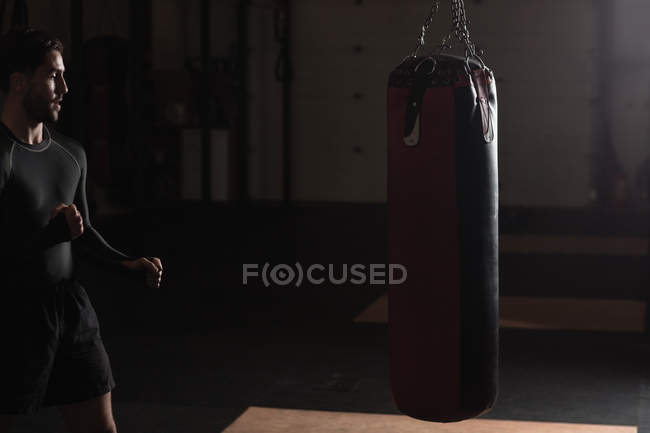 Boxer masculino praticando boxe com saco de perfuração no estúdio de fitness — Fotografia de Stock