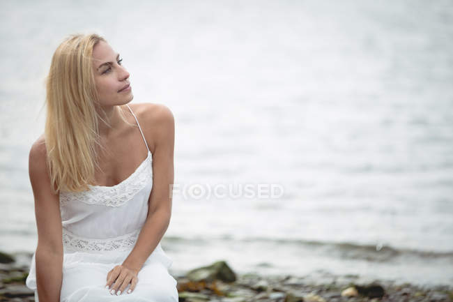 Carefree blonde woman crouching near river and looking away — Stock Photo