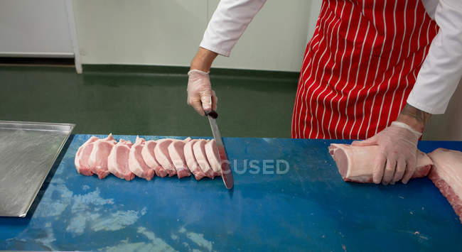 Sección media del carnicero rebanando carne en la carnicería - foto de stock