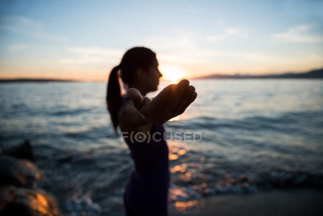 Foco seletivo da mulher praticando ioga na praia durante o pôr do sol — Fotografia de Stock