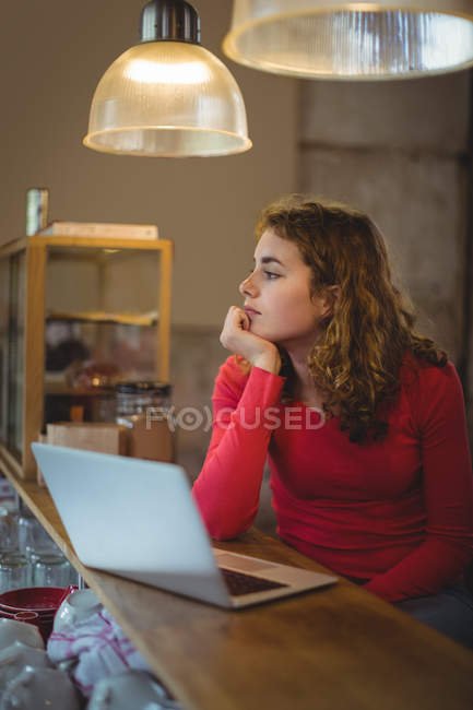 Mujer pensativa sentada en el mostrador con el ordenador portátil en la tienda de bicicletas - foto de stock