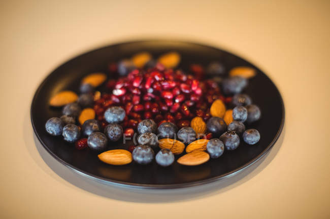 Granatapfel, Blaubeere und Mandeln in einem Teller auf Holztisch — Stockfoto