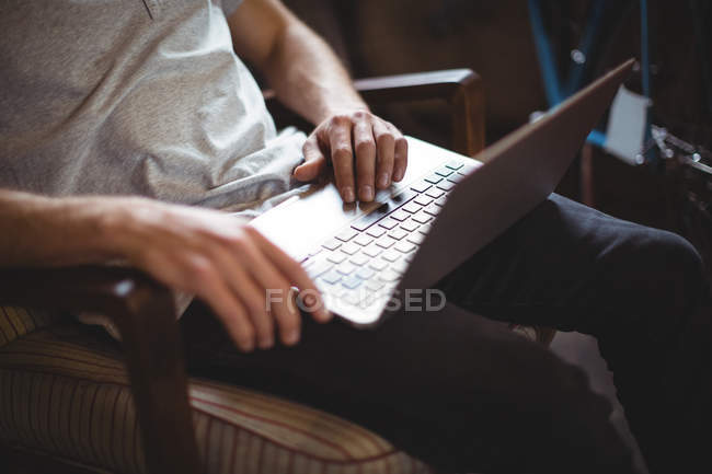 Средняя часть человека, сидящего на стуле и использующего ноутбук в магазине велосипедов — стоковое фото
