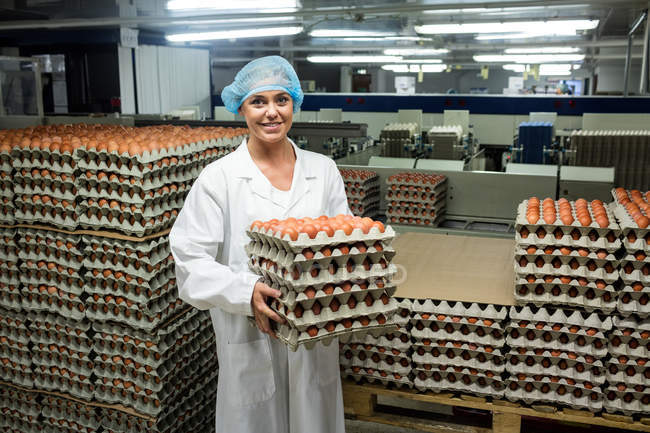 Portrait of female staff holding egg trays in factory — Stock Photo