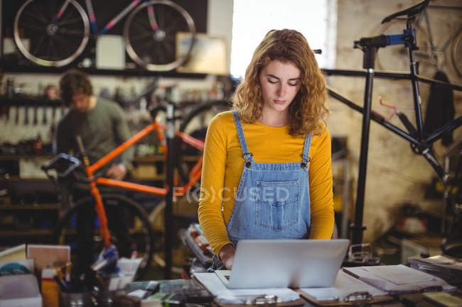 Mechanic using laptop at counter in bicycle shop — Stock Photo