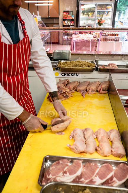 Sección media del carnicero picando pollo en el mostrador de trabajo en la carnicería - foto de stock