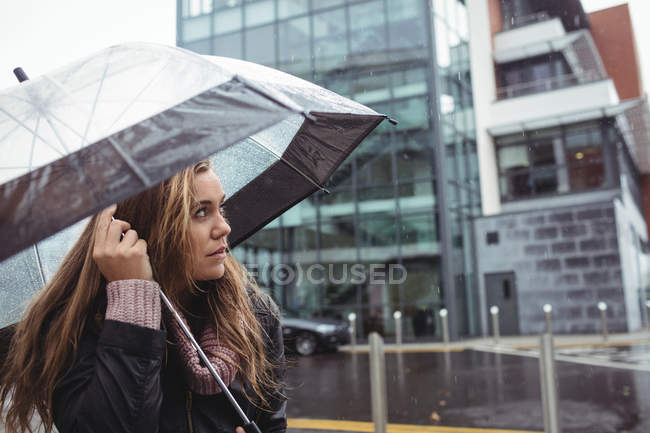 Schöne Frau mit Regenschirm während der Regenzeit auf der Straße — Stockfoto