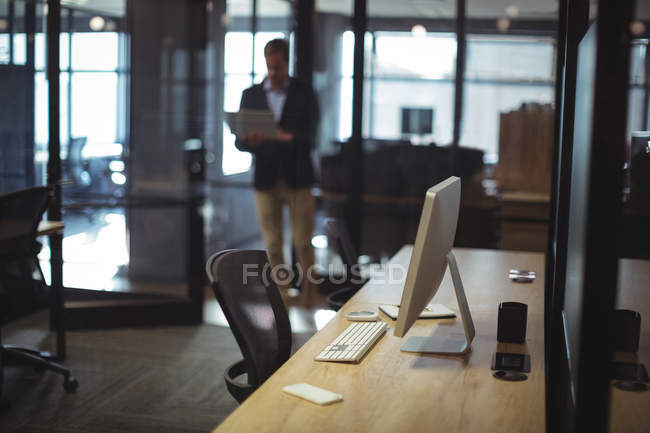 Mesa com PC desktop e homem de negócios usando laptop no escritório — Fotografia de Stock