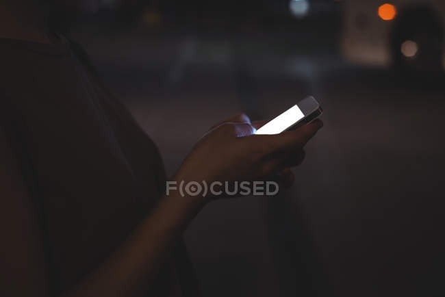 Mid section of woman using mobile phone on street at night — Stock Photo