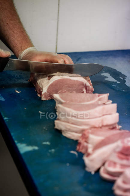 Manos de carnicero picando carne en el mostrador de trabajo en la carnicería - foto de stock
