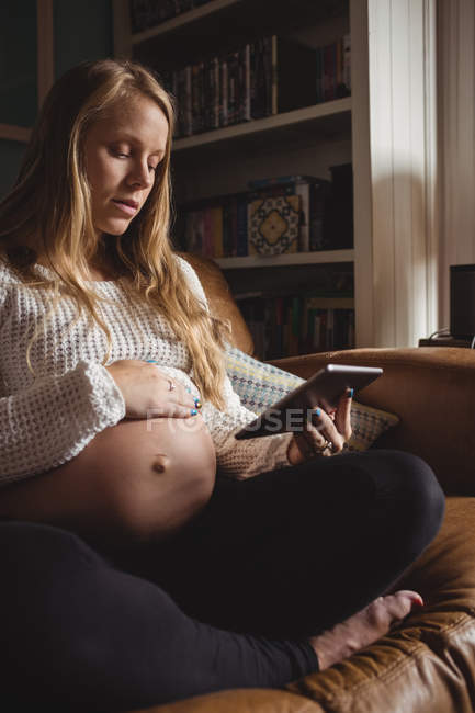 Беременная женщина, использующая цифровой планшет в гостиной дома — стоковое фото