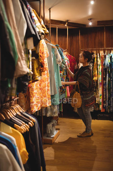 Женщина выбирает одежду на вешалках в магазине одежды — стоковое фото