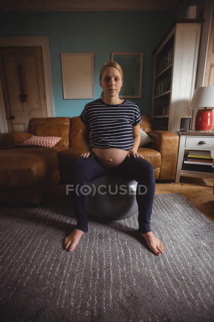 Retrato de mulher grávida sentada na bola de exercício na sala de estar em casa — Fotografia de Stock