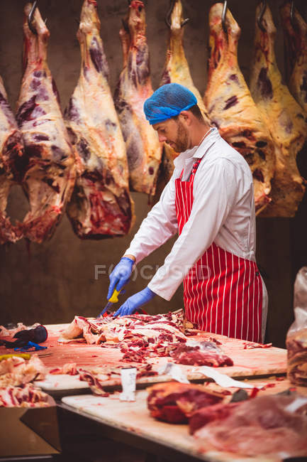 Мясник режет мясо на складе мясной лавки. — стоковое фото