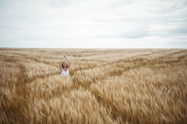 Жінка з піднятими руками над головою в молитовній позиції, стоячи на полі в сонячний день — стокове фото