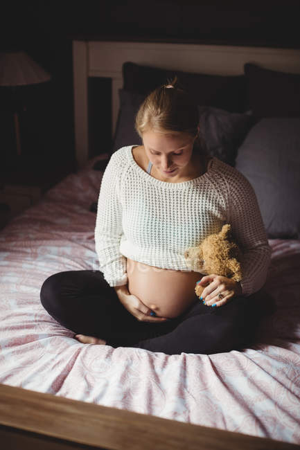 Беременная женщина держит плюшевого мишку в спальне дома — стоковое фото
