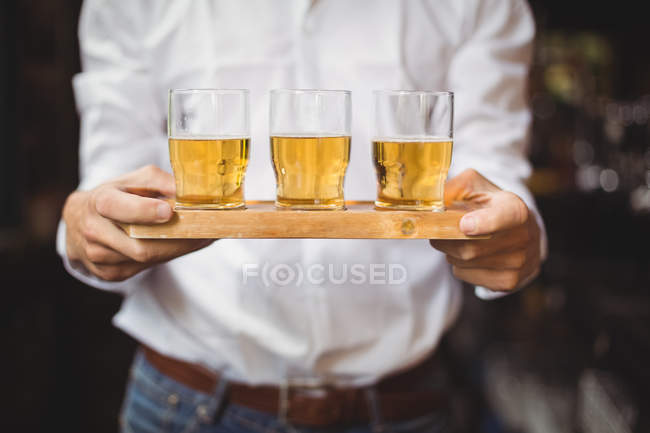 Mid section of bartender holding tray of whisky shot glasses at bar counter in bar — Stock Photo