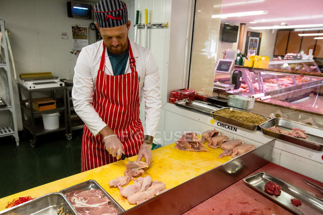Carnicero picando pollo en el mostrador de trabajo en la carnicería - foto de stock