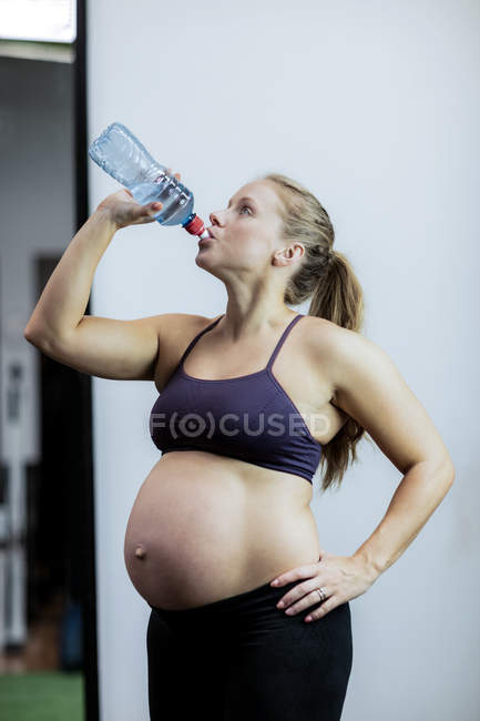 Беременная женщина пьет воду во время перерыва в спортзале — стоковое фото