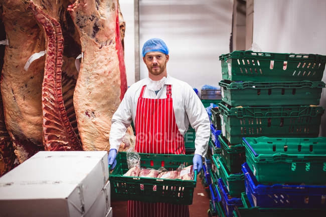 Retrato del carnicero que lleva una caja de carne roja en el almacén de la carnicería - foto de stock