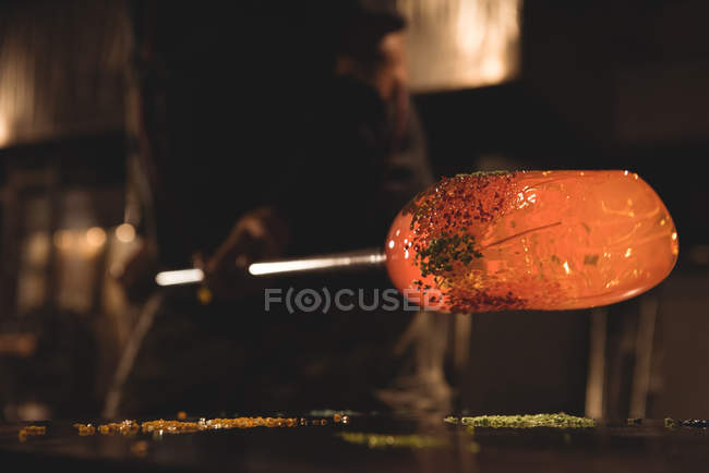 Close-up of glassblower rolling molten glass on pieces of colored glass at glassblowing factory — Stock Photo