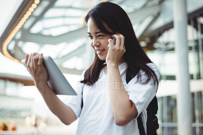 Jeune femme parlant sur un téléphone portable tout en utilisant une tablette numérique — Photo de stock