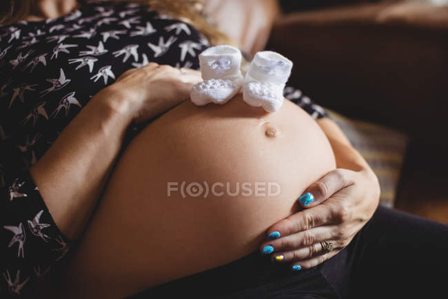 Abgeschnittenes Bild von Baby-Socken auf Schwangerschaftsbauch zu Hause — Stockfoto