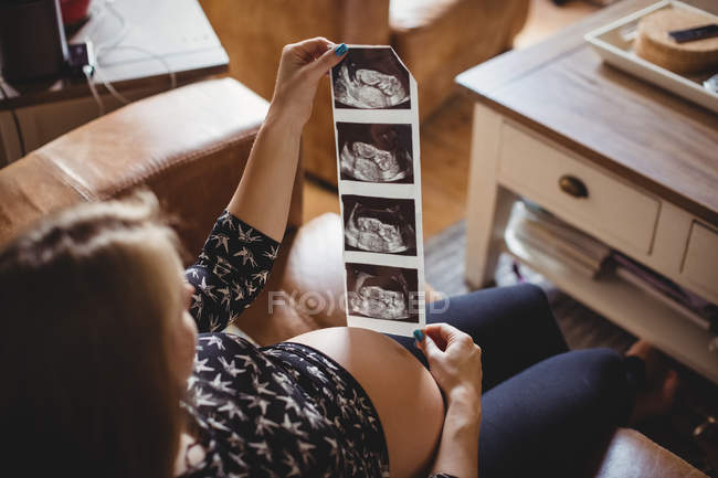 Femme enceinte regardant une échographie dans le salon à la maison — Photo de stock