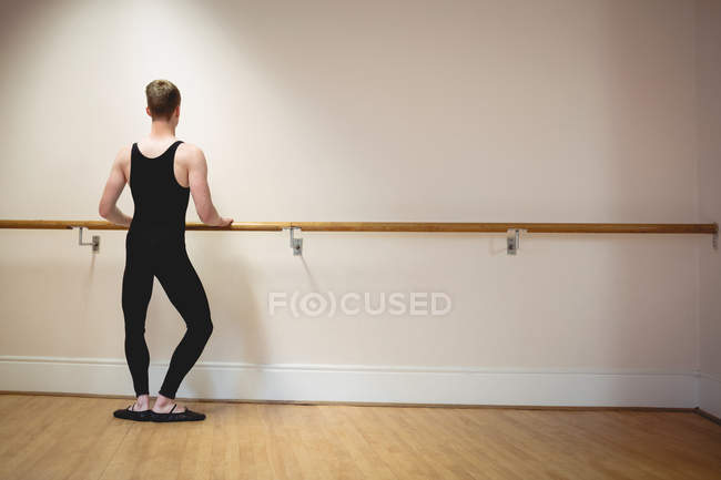 Вид сзади на растяжение Балерино на барре во время репетиции балетного танца в студии — стоковое фото
