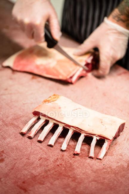 Manos de carnicero cortando costillas de cerdo en la carnicería - foto de stock