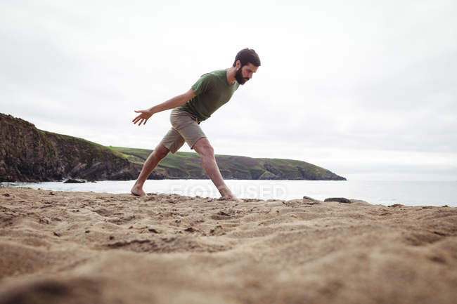 Hombre realizando ejercicio de estiramiento en la playa - foto de stock