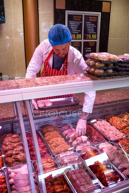 Carnicero revisando la exhibición de carne en la carnicería - foto de stock