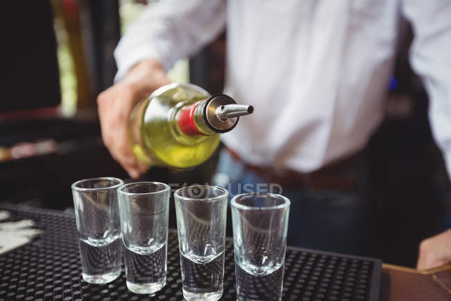 Close-up de bartender derramando tequila em copos de tiro no balcão de bar no bar — Fotografia de Stock
