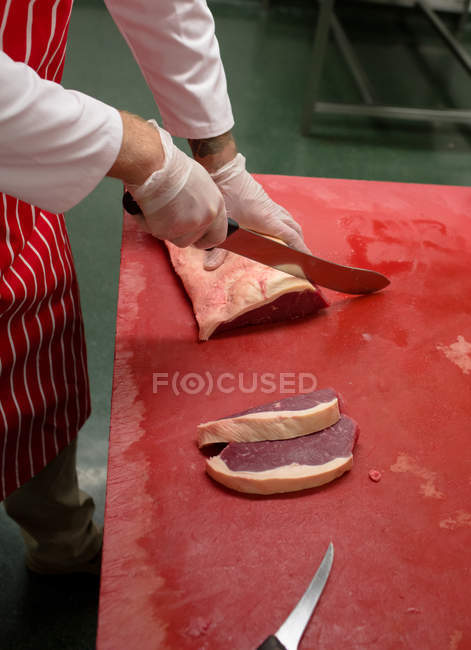 Mani di macellaio affettare carne rossa in macelleria — Foto stock