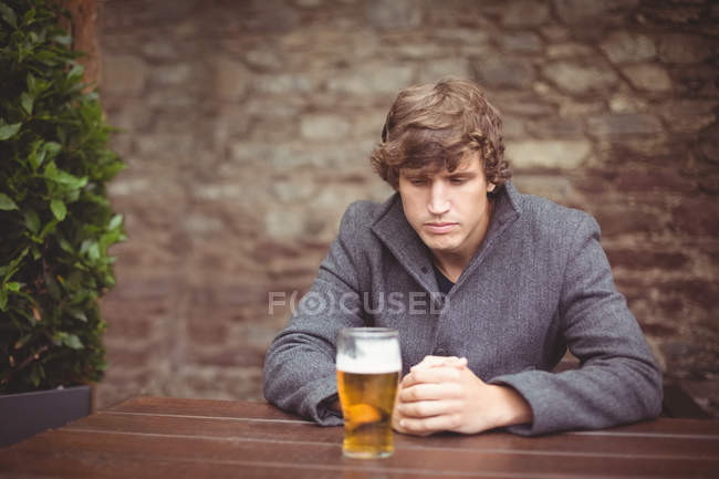 Нещасний чоловік сидить у барі зі склянкою пива на столі — стокове фото