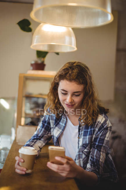 Mecânico usando telefone celular enquanto toma café no balcão na oficina — Fotografia de Stock