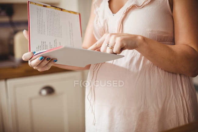 Abgeschnittenes Bild einer schwangeren Frau, die zu Hause in der Küche Buch liest — Stockfoto