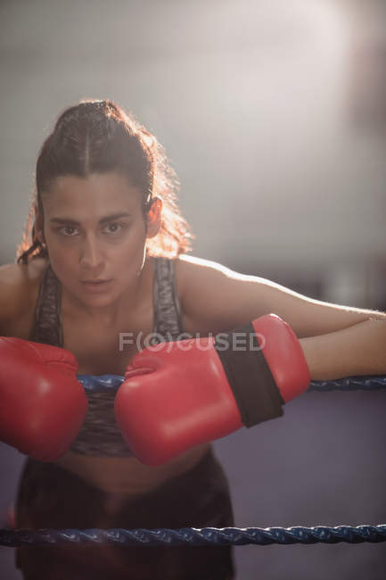 Portrait of female boxer in gloves leaning on boxing ring rope at fitness studio — Stock Photo