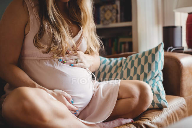 Обрізане зображення вагітної жінки, що розслабляє і зворушує живіт у вітальні — стокове фото